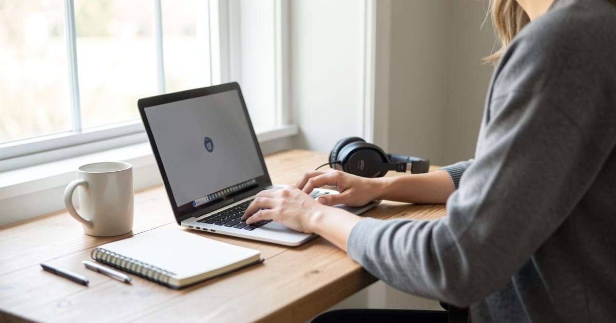 Person working on a laptop at a tidy home desk beside a sunny window